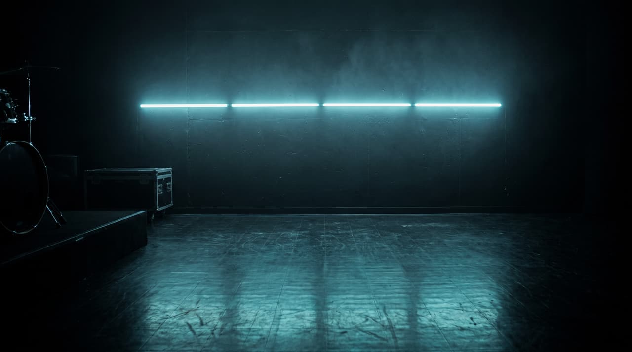 A black rehearsal room lit by one teal neon tube reflecting on the floor